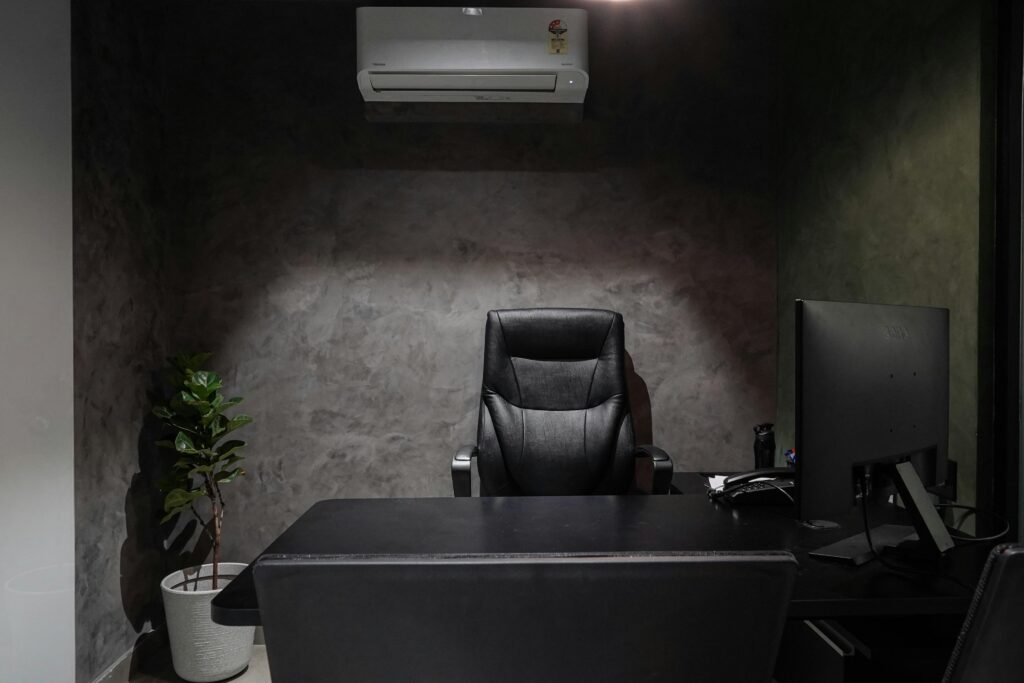 pexels-photo-18495294-18495294 Minimalist office interior featuring leather chair, desk, monitor, plant, and air conditioner.