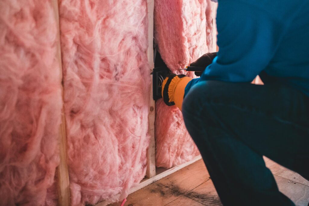 pexels-photo-6124239-6124239 Focused worker installing pink fiberglass insulation in a building interior.