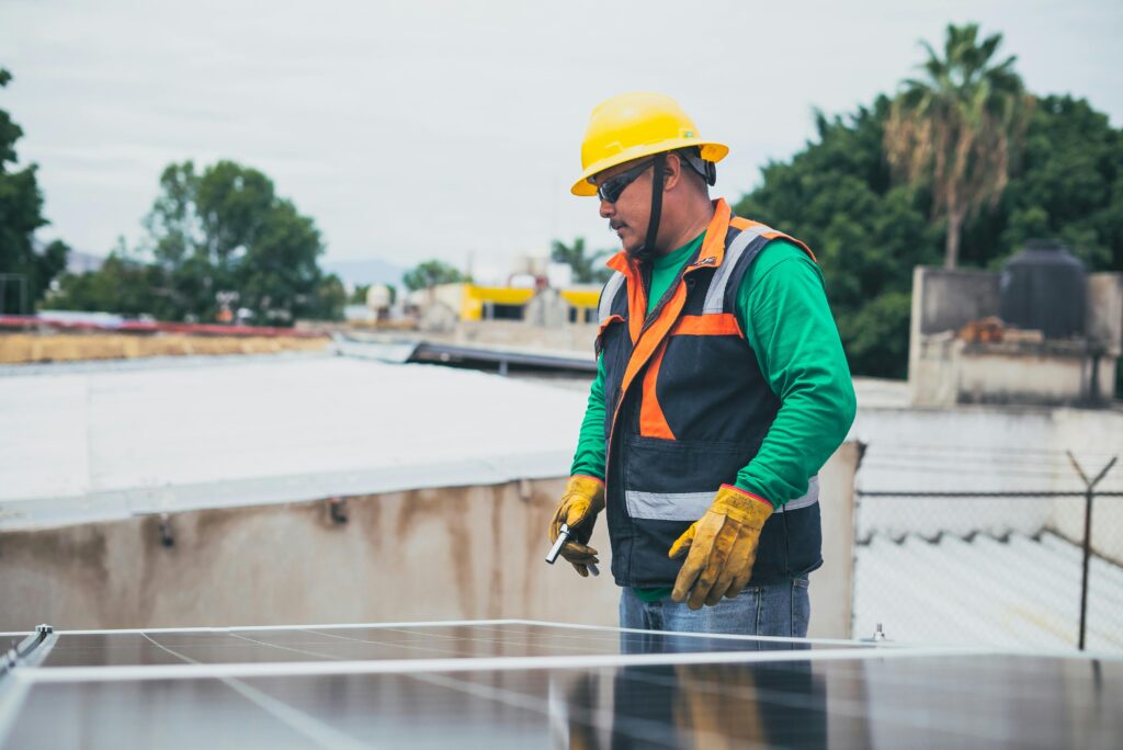 pexels-photo-8853512-8853512 A solar technician in protective gear inspecting rooftop solar panels outdoors.