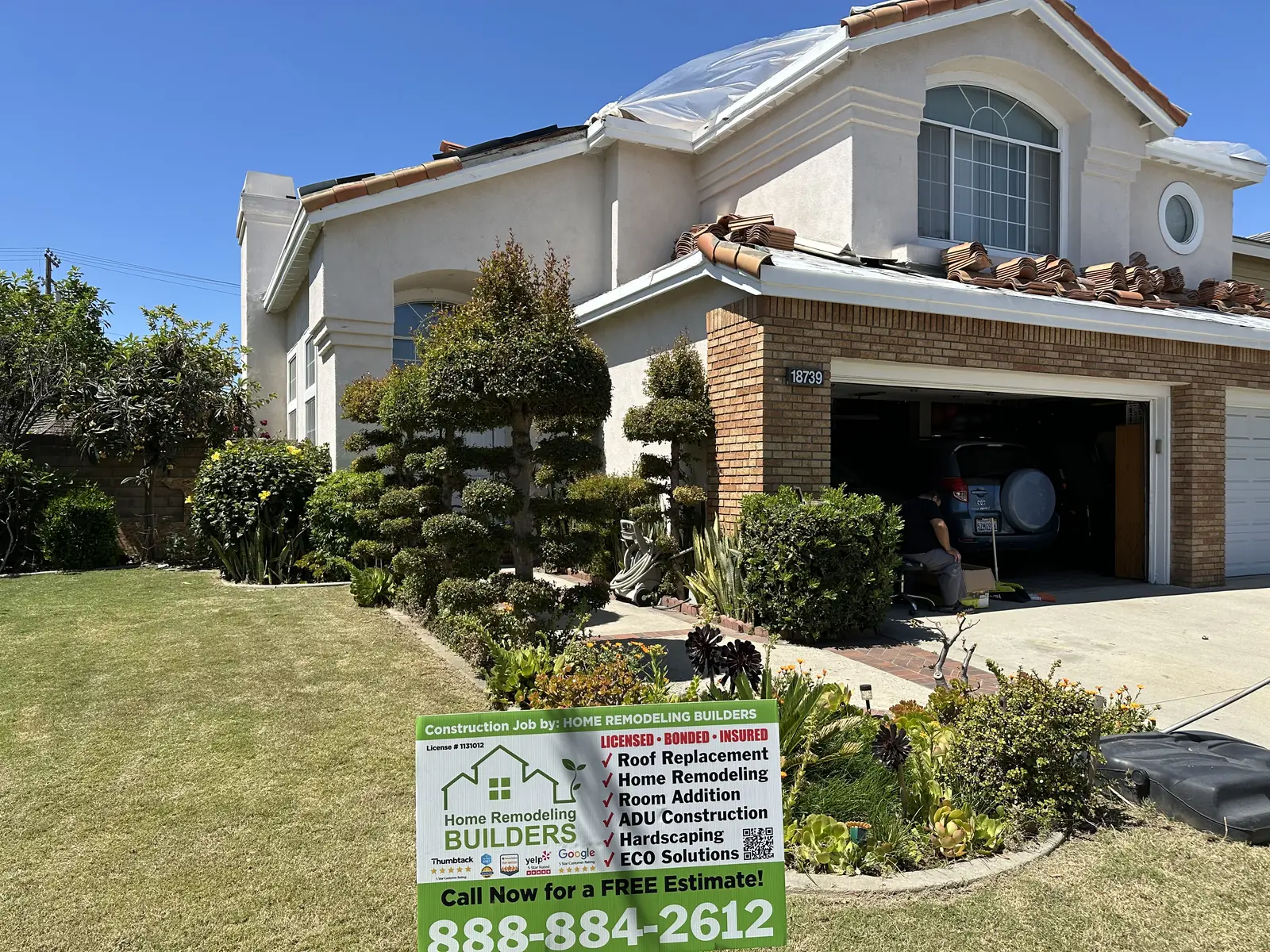 Tiles staged above the garage, with the company sign in the foreground. Cerritos roofing project.