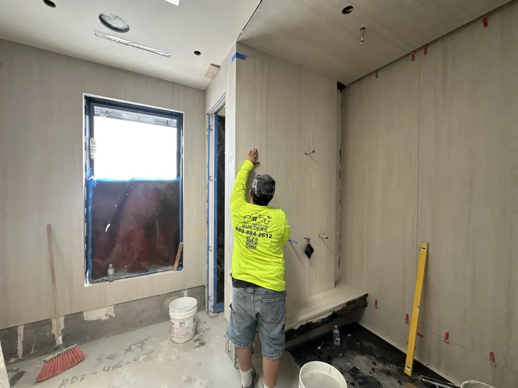 A crew member in a branded shirt checks the upper bathroom wall tile.