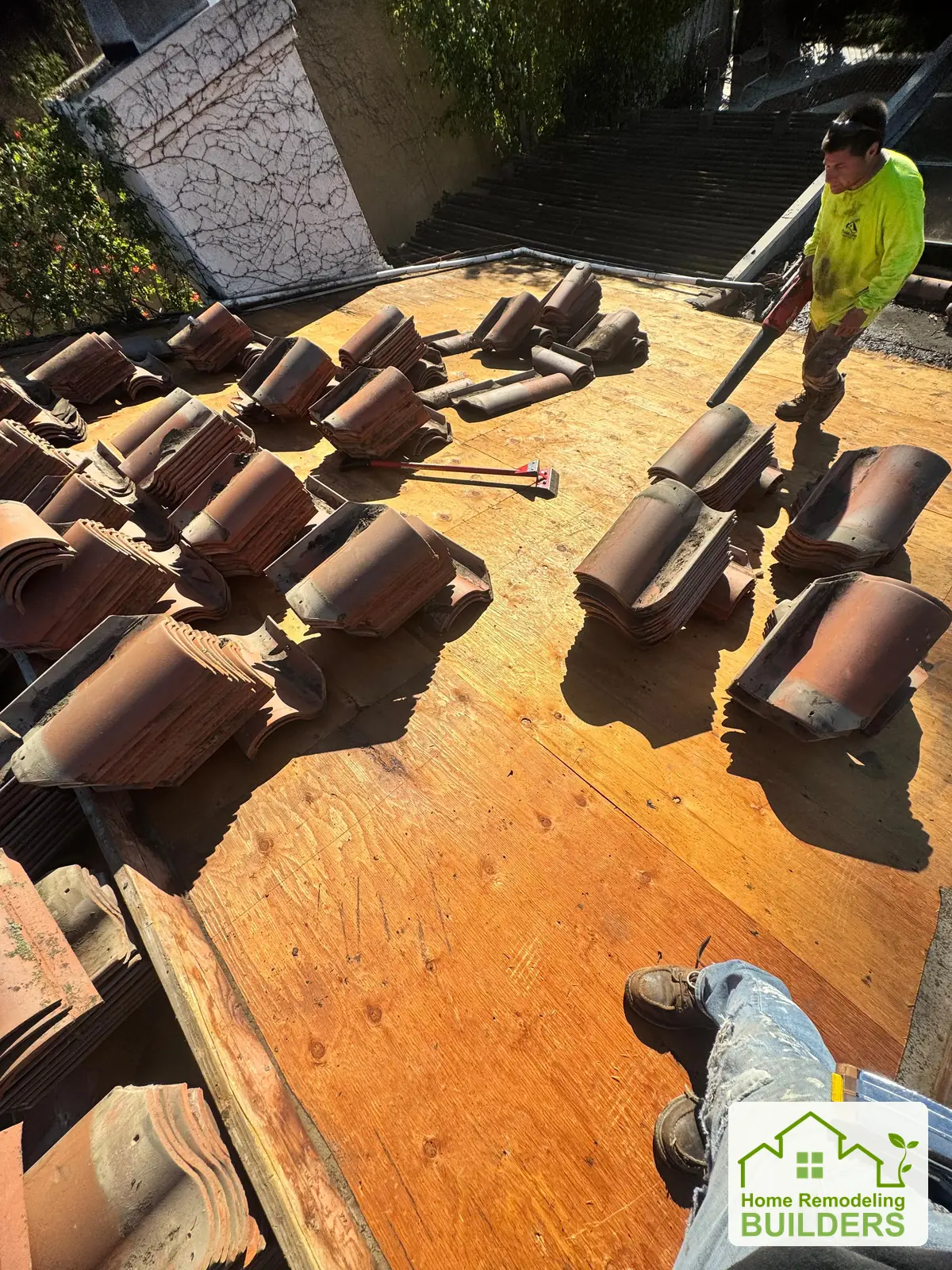 A crew member works on the exposed deck beside staged tiles. Laguna Hills roofing project.