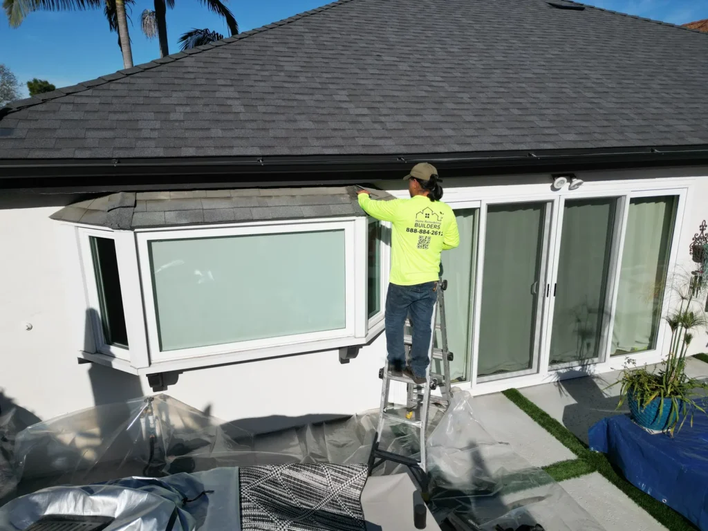 A team member in a branded Home Remodeling Builders shirt works along the eave. Santa Ana roofing project.
